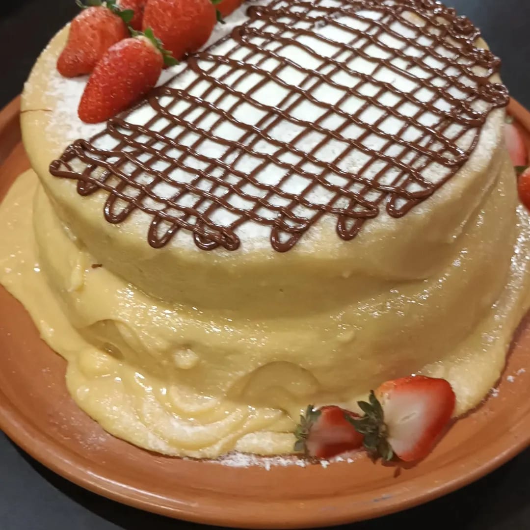 bolo de dois andares com cobertura amarela, morangos e raspas de chocolate em um prato laranja