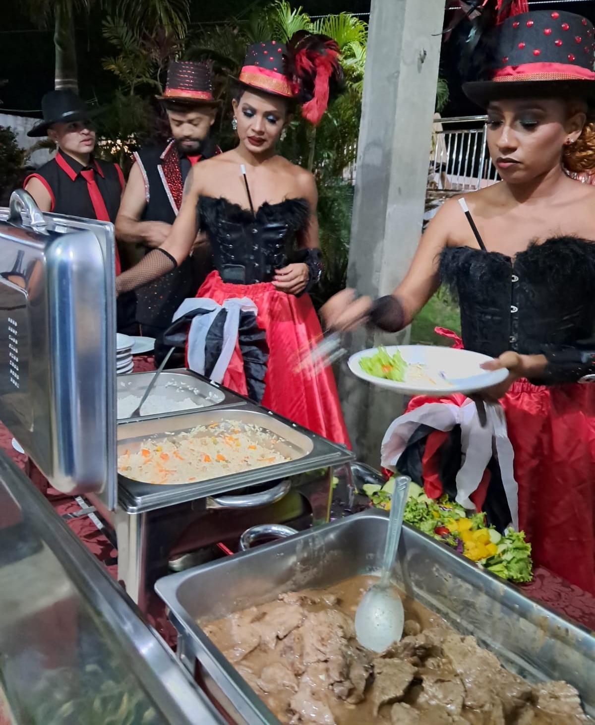 equipe de buffet tematicamente fantasiada com cartolas vermelhas e pretas servindo comida em rechações durante